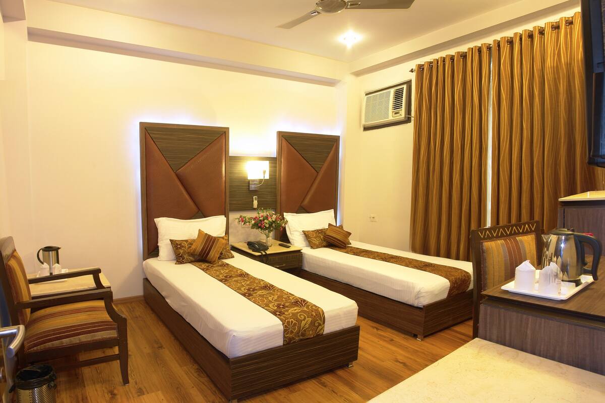 A hotel room with two single beds, a desk with a chair, a ceiling fan, and a large window with curtains.