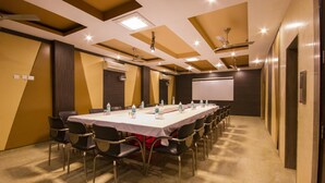 Un salón de conferencias con una mesa larga, sillas, una pantalla de proyector y una pizarra.