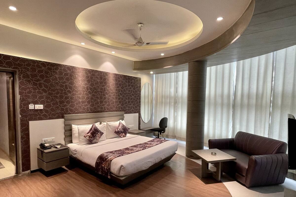 A modern hotel room with a large bed, a desk, a chair, and a large window with curtains.