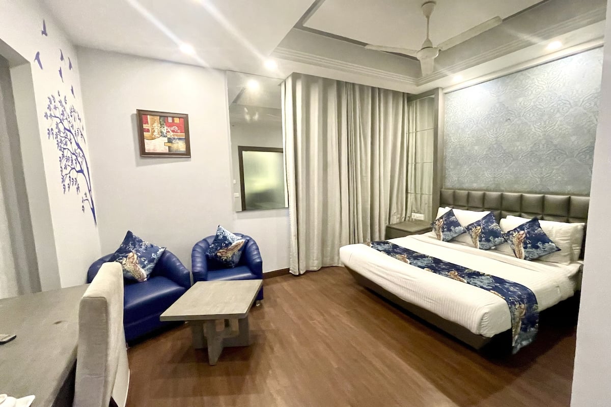 A modern hotel room with a bed, a sofa, a small table, and a window with curtains.