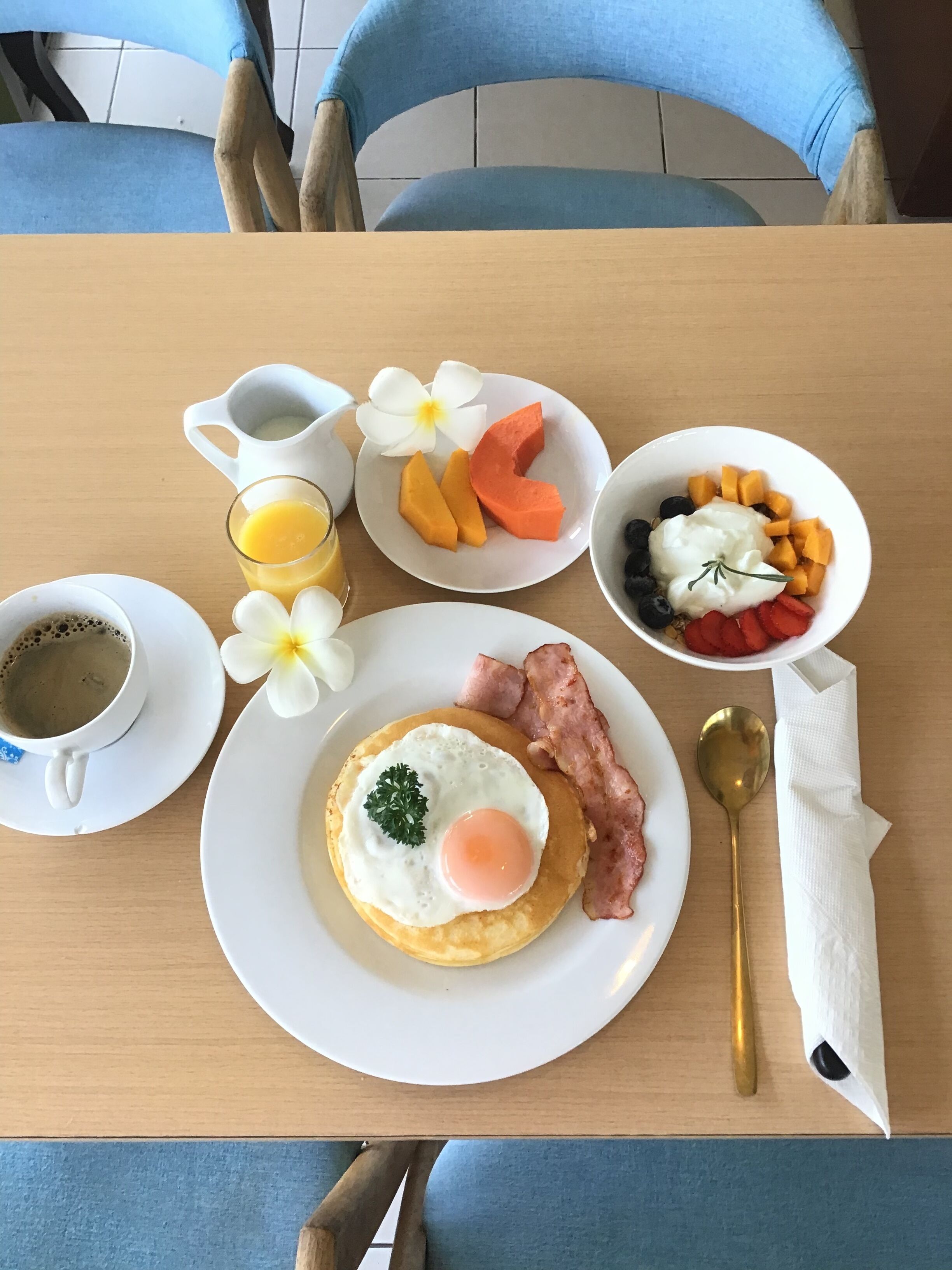 A breakfast table with a plate of eggs, bacon, and fruit, a glass of orange juice, and a coffee cup.