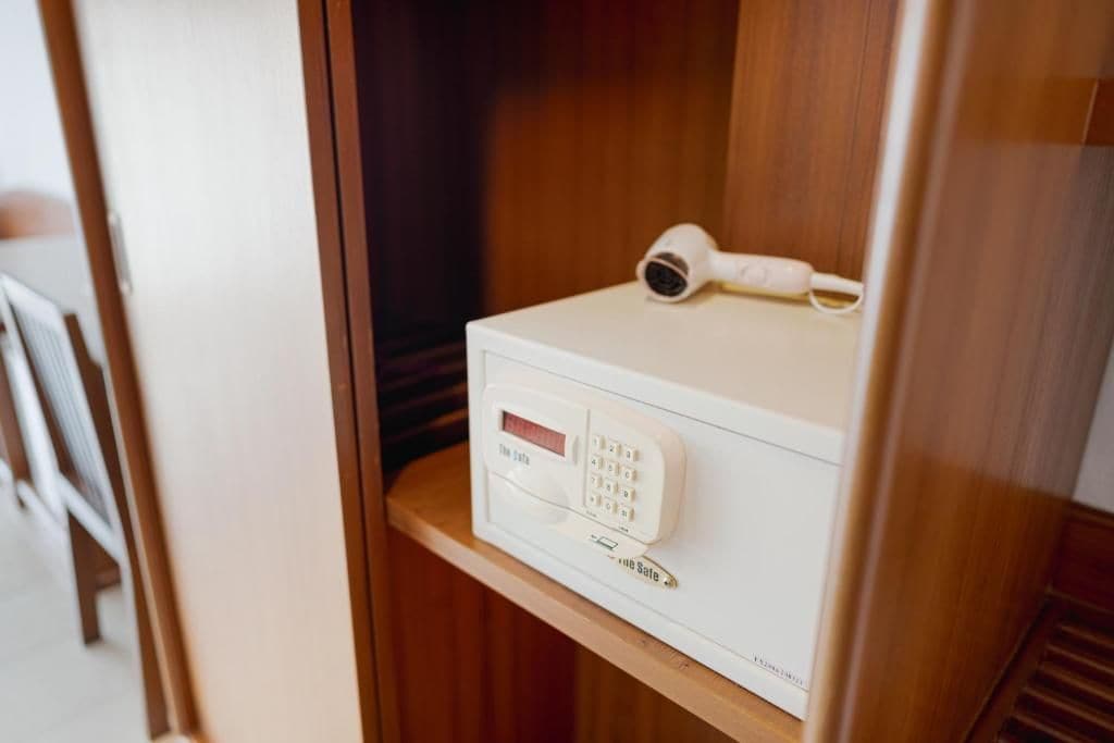 Un dispositivo electrónico blanco con teclado y una pantalla pequeña, posiblemente un panel de control o un dispositivo de seguridad, sobre una estantería de madera.