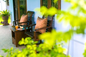A wooden bench with a cushion, a small table with a cup and a book, and a potted plant in the background. - My Village Lamai (Koh Samui)