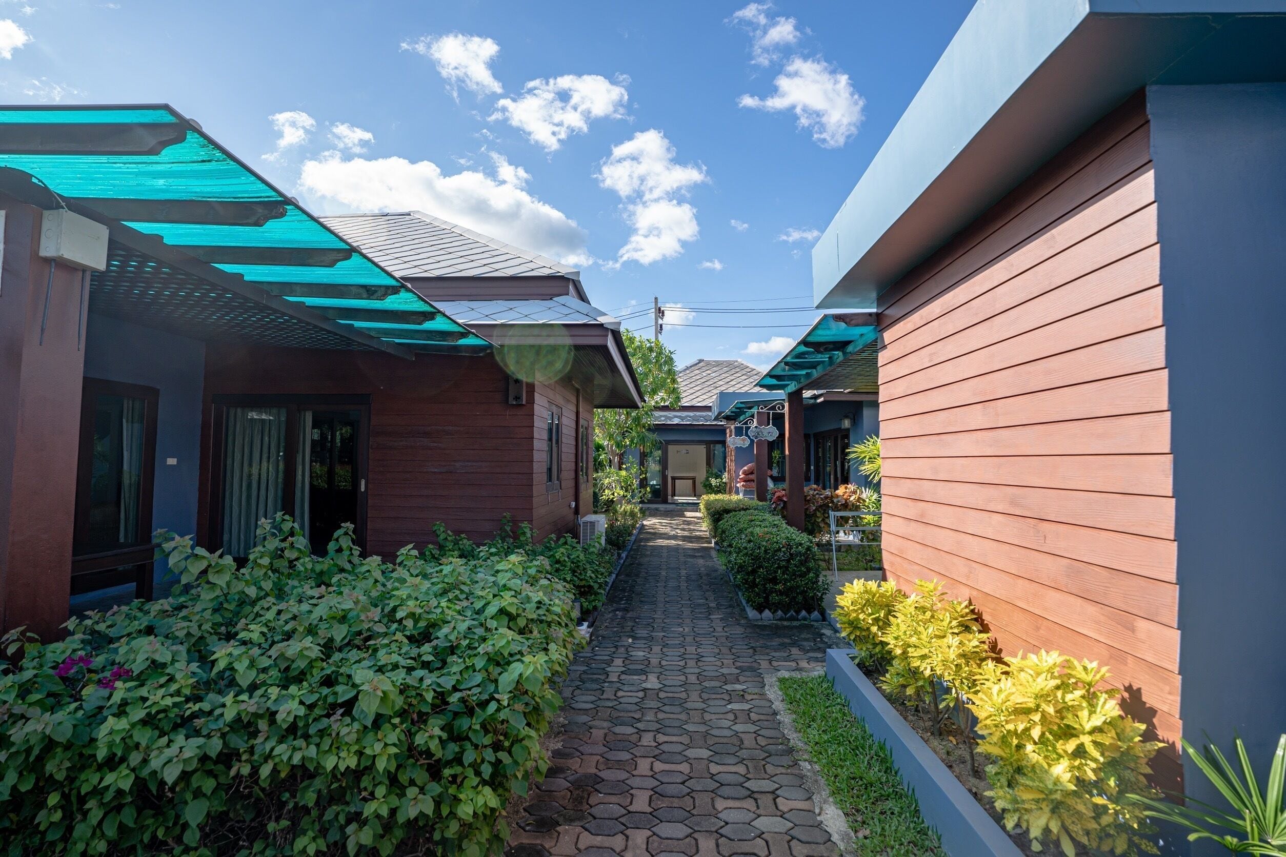 Un sendero que atraviesa una zona residencial con casas modernas, cielo despejado y abundante vegetación cuidada.