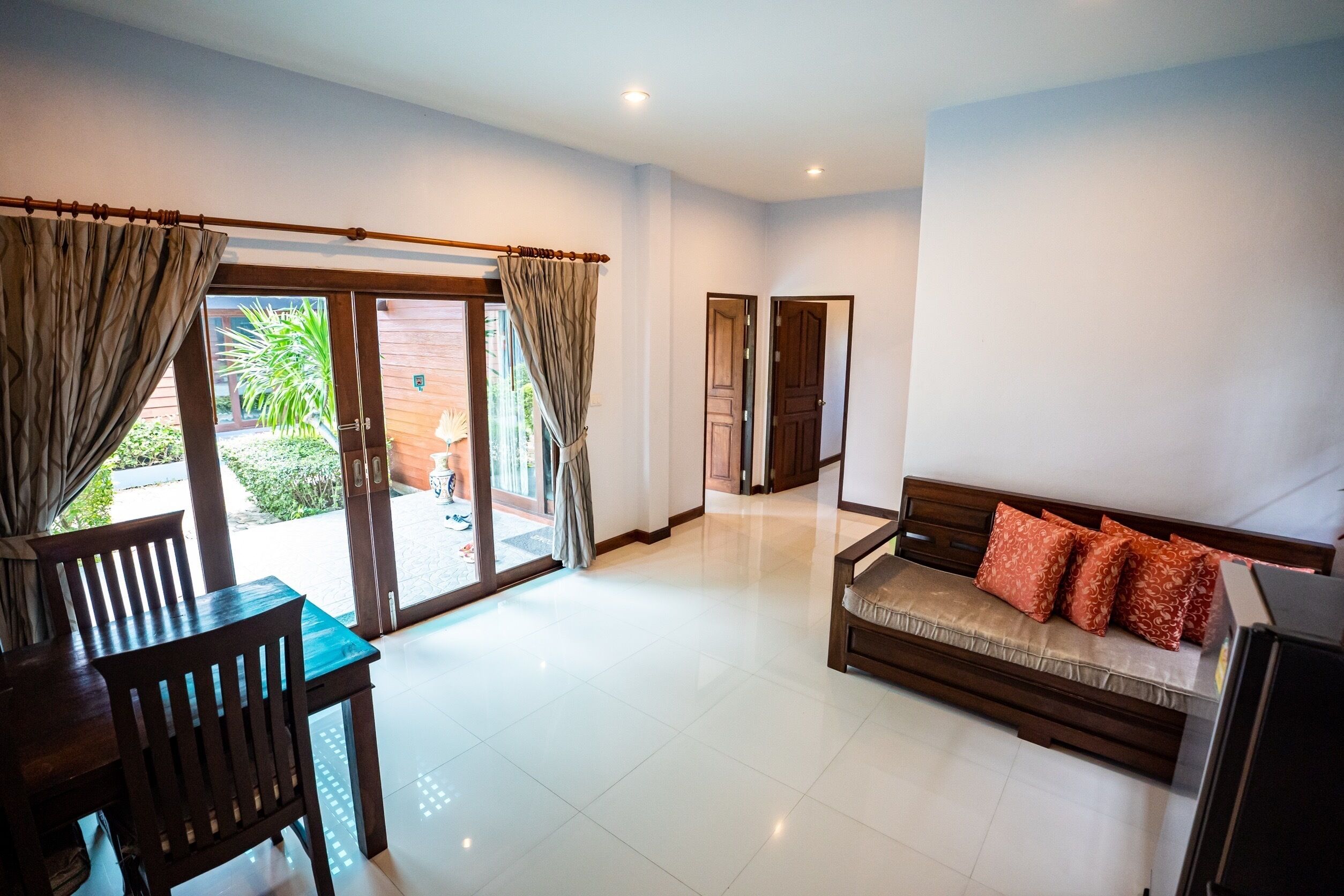 A spacious living area with a sofa, a dining table, and chairs, a sliding glass door leading to an outdoor area, and a wooden door in the background.