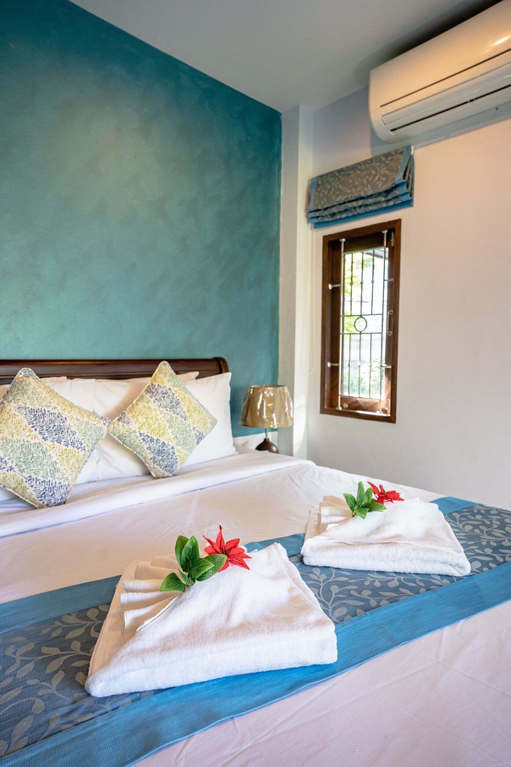 A hotel room with a bed, pillows, a window, and an air conditioning unit.