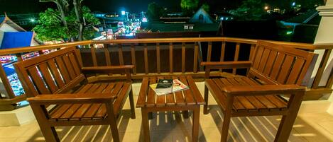 Un banc et une table en bois sont installés sur un balcon, d’où l’on peut admirer une zone illuminée au loin.