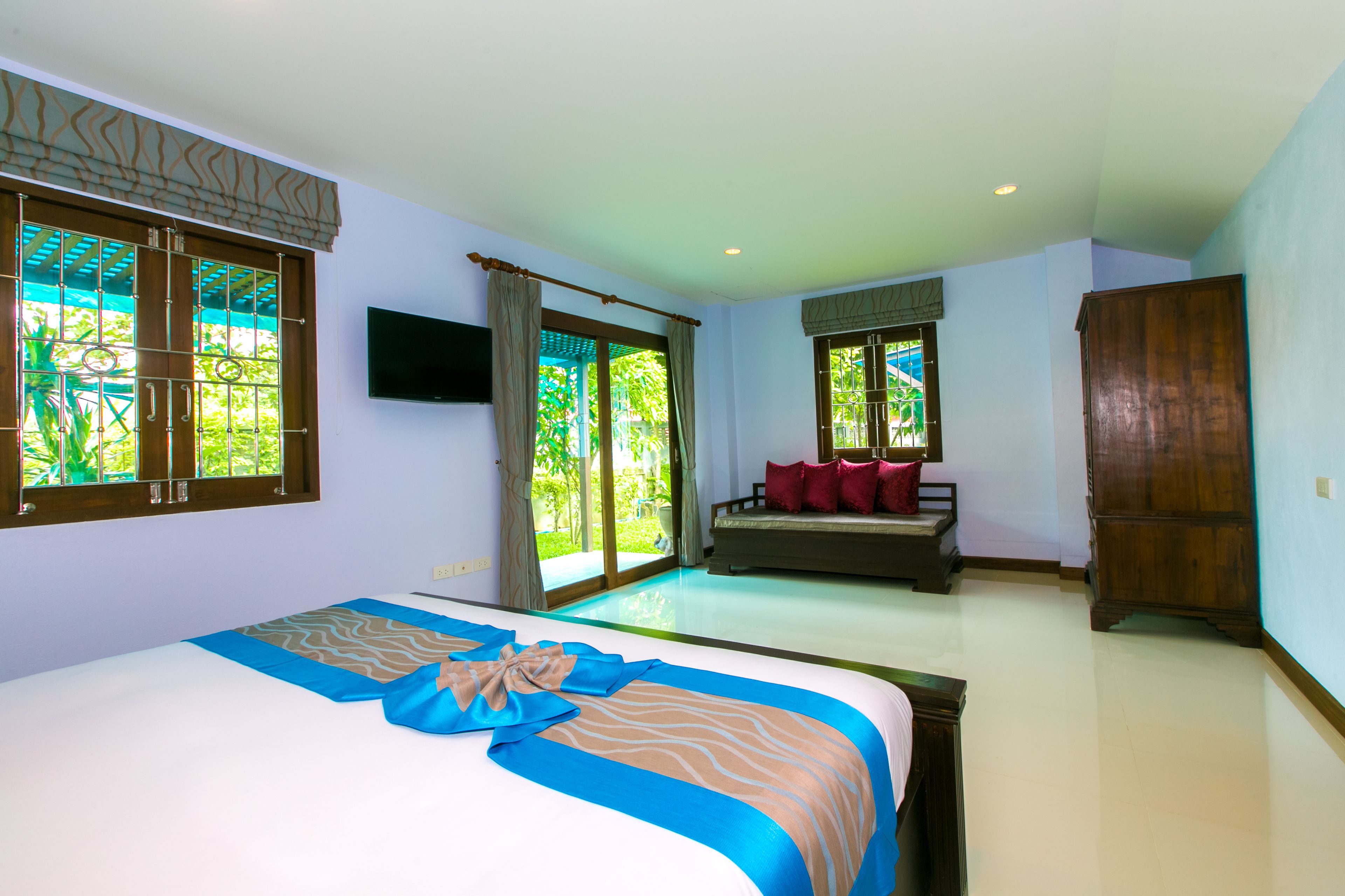 A hotel room with a large bed, a sofa, a TV, and a wooden wardrobe.