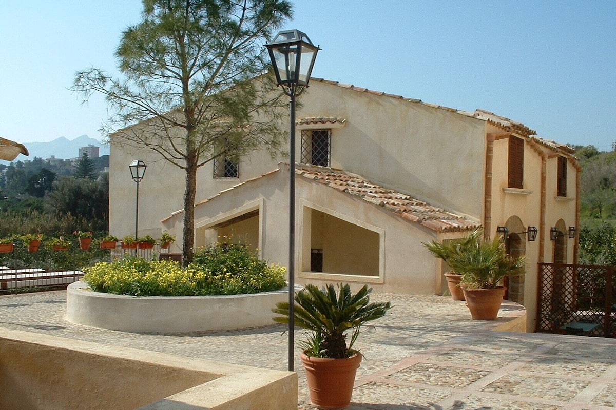 A building with a tiled roof, a central entrance, and a landscaped courtyard with potted plants.