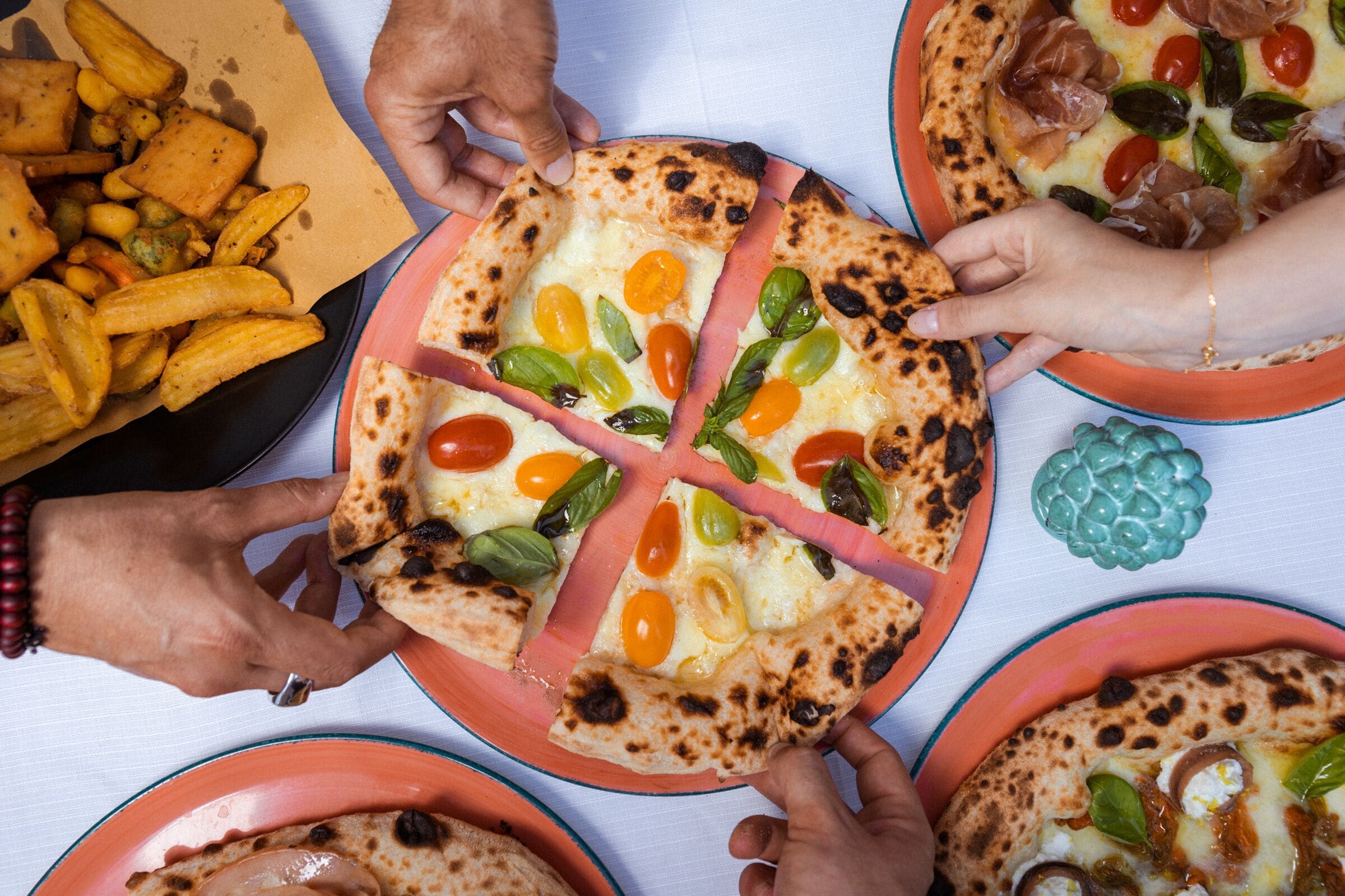 A group of people sharing a meal with pizza and fries.