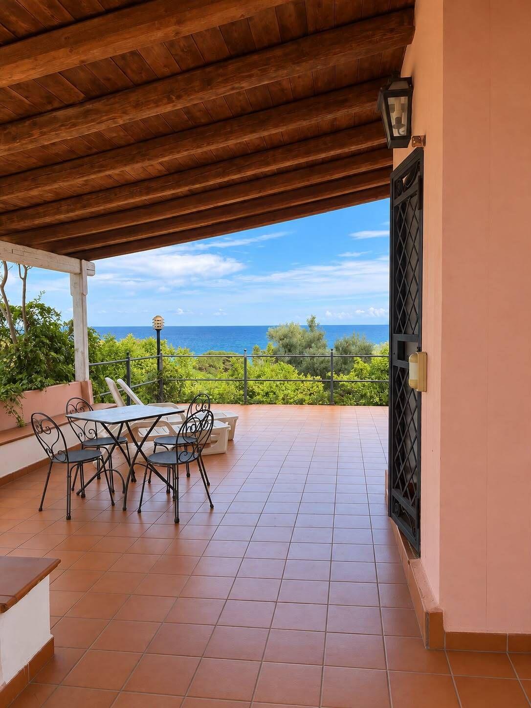 Une terrasse extérieure avec une table et des chaises, une vue sur la mer et un plafond en bois.