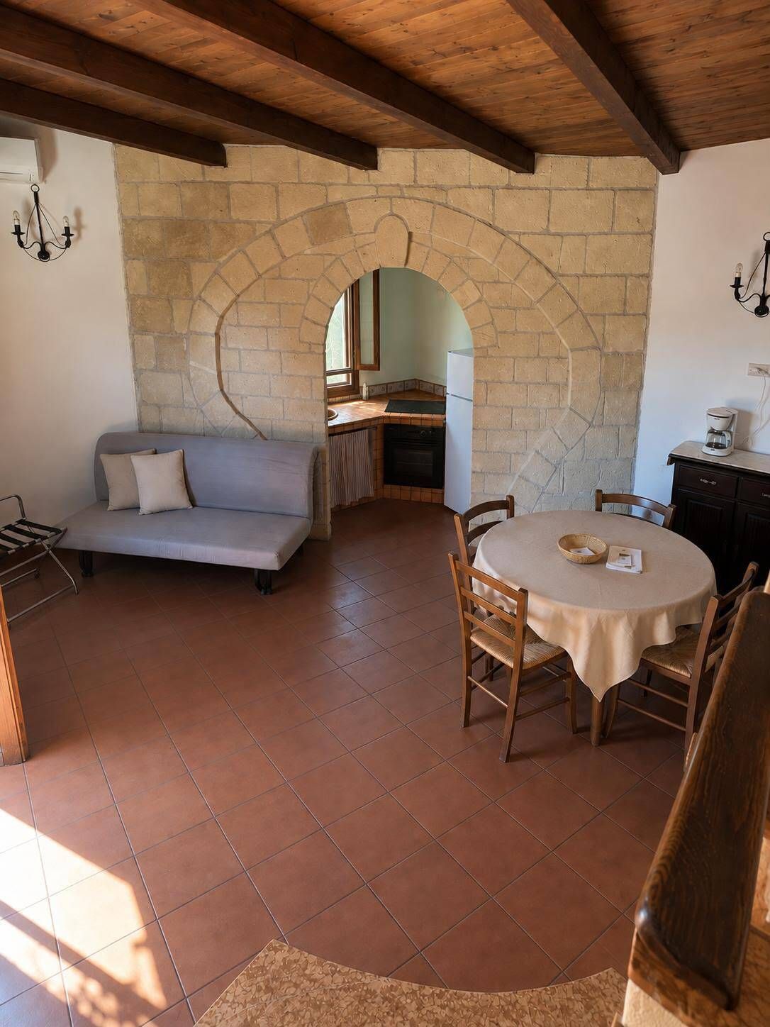 A cozy interior with a stone archway, a dining table with chairs, a sofa, and a kitchen area.
