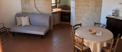A cozy interior with a stone archway, a dining table with chairs, a sofa, and a kitchen area.