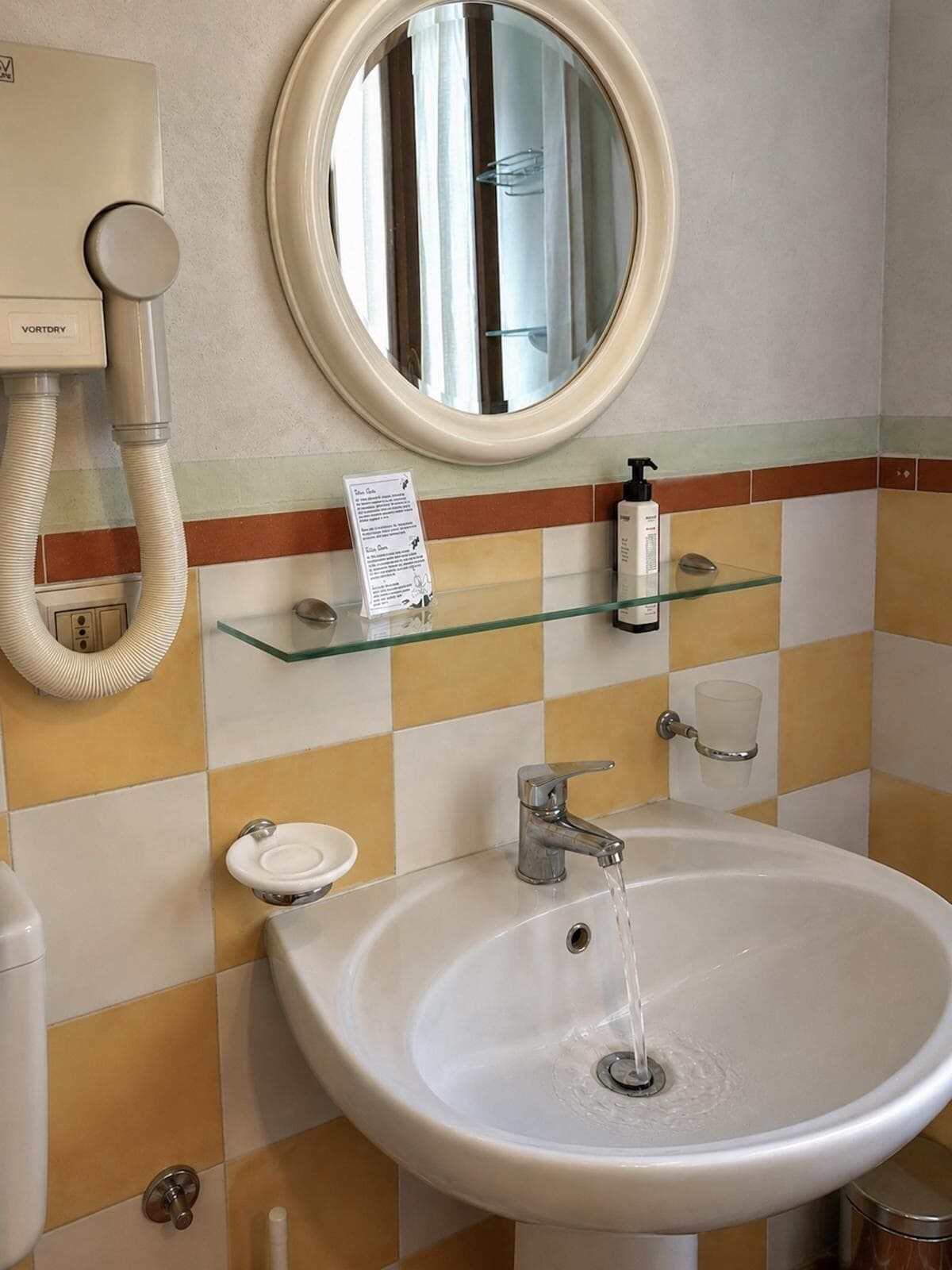 Un baño con lavamanos, espejo, toallero y secador de manos.
