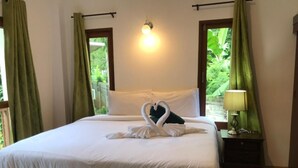 A neatly made bed with white linens and a swan-shaped towel arrangement. There is a bedside lamp on a wooden nightstand. - Green Villa (Koh Samui)