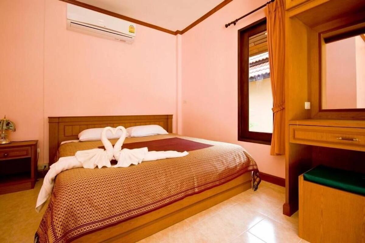 Une chambre d’hôtel comprenant un lit, une tête de lit en bois, une table de chevet, une commode et un appareil de climatisation.