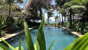 A pool surrounded by tropical plants and palm trees, with a view of the sea in the background. - Full Moon Beach (Mui Ne)