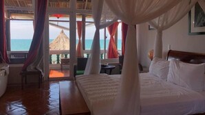 A bedroom with a bed, a nightstand, a chair, and a view of the ocean through large windows. - Full Moon Beach (Mui Ne)