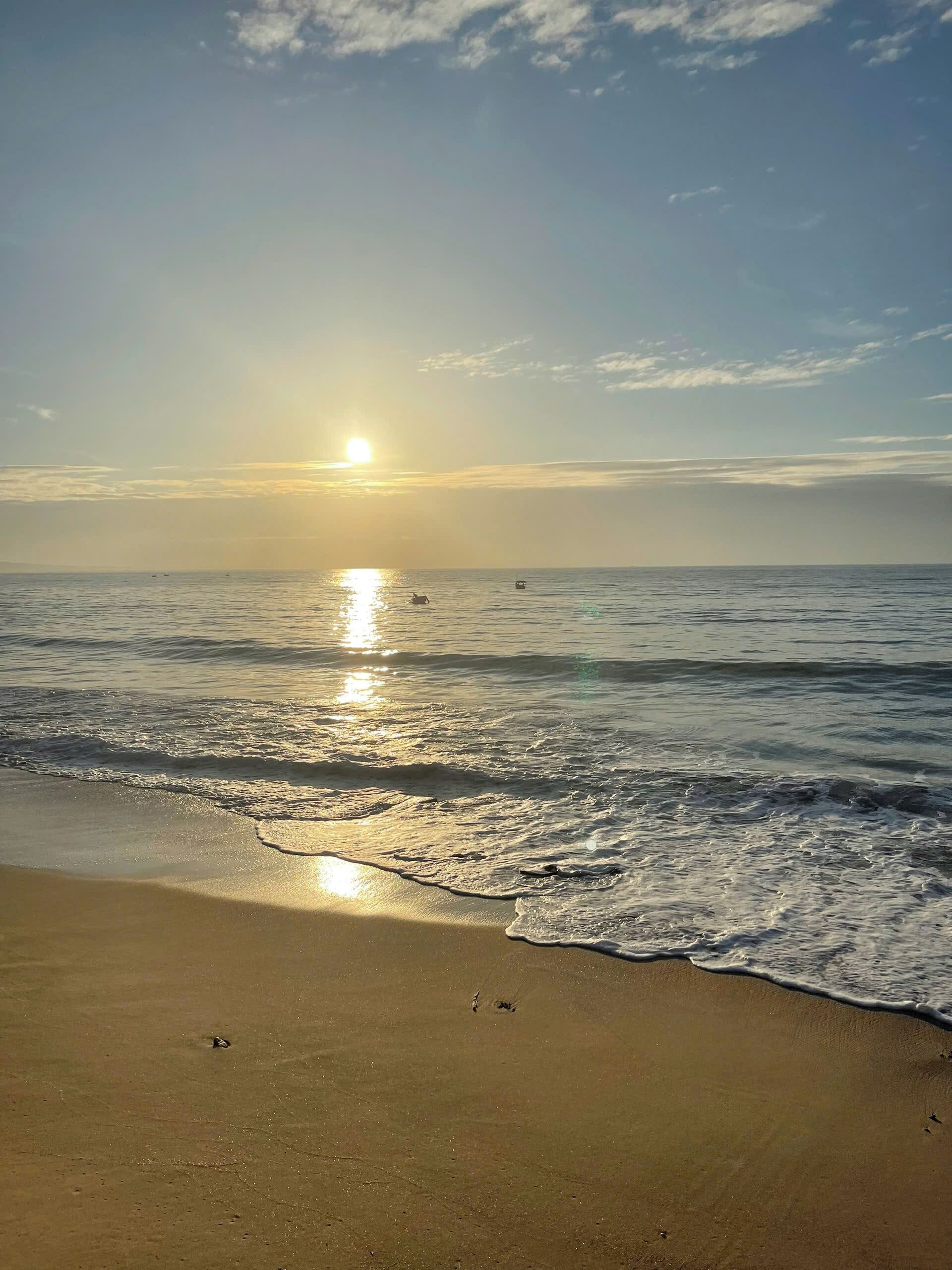 Une plage où le soleil se couche sur l’océan, et où les vagues viennent doucement lécher le rivage.