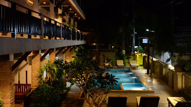 A nighttime view of a hotel courtyard with a swimming pool, lounge chairs, and potted plants. - Vanda House Resort (Koh Samui)