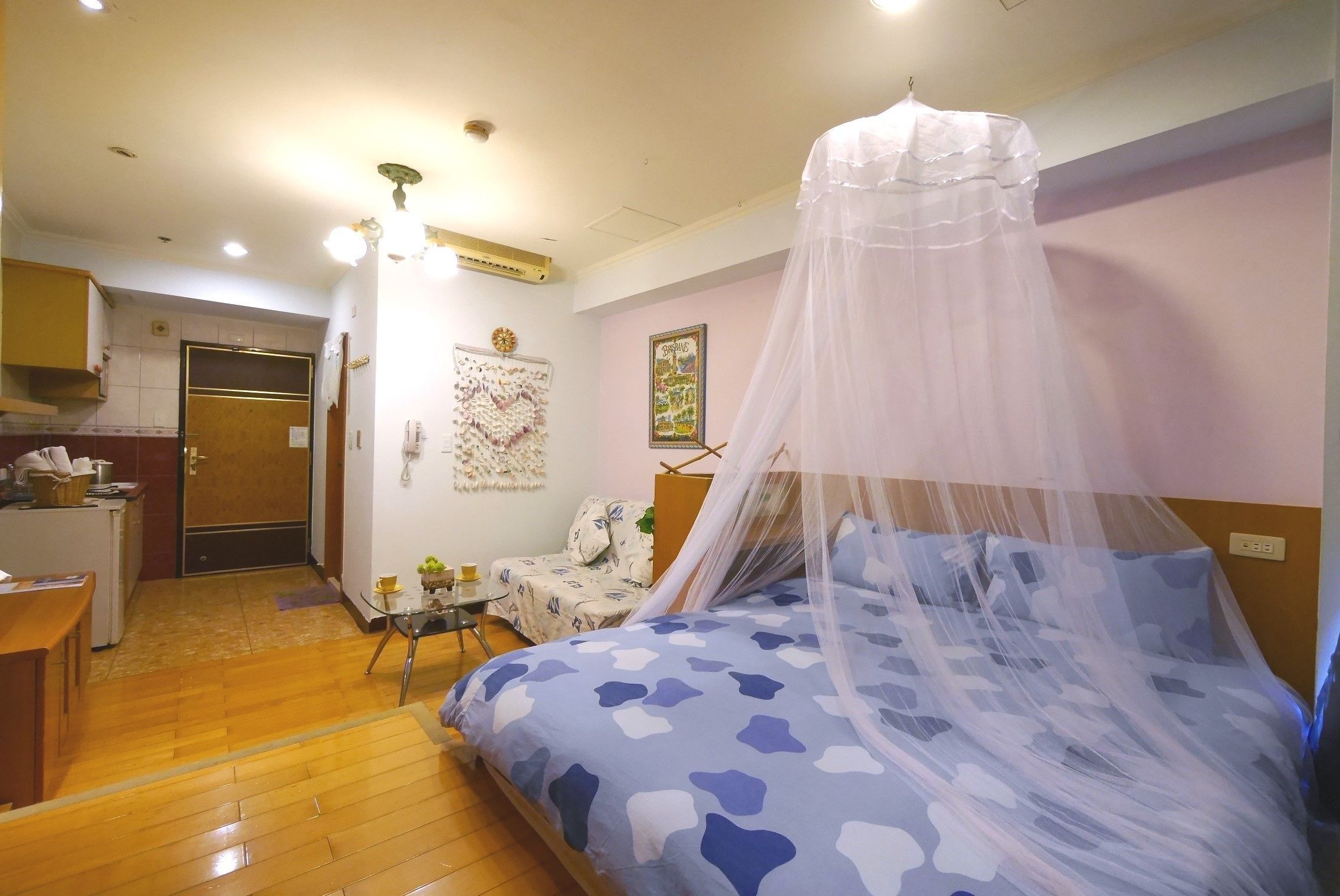 Un dormitorio con una cama bajo un dosel, un escritorio con silla, una mesita y una zona de kitchenette.