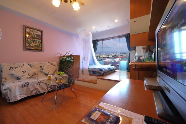 A modern living room with a sofa, a glass coffee table, a TV, and a large window offering a city view. - Each Family (Kaohsiung)