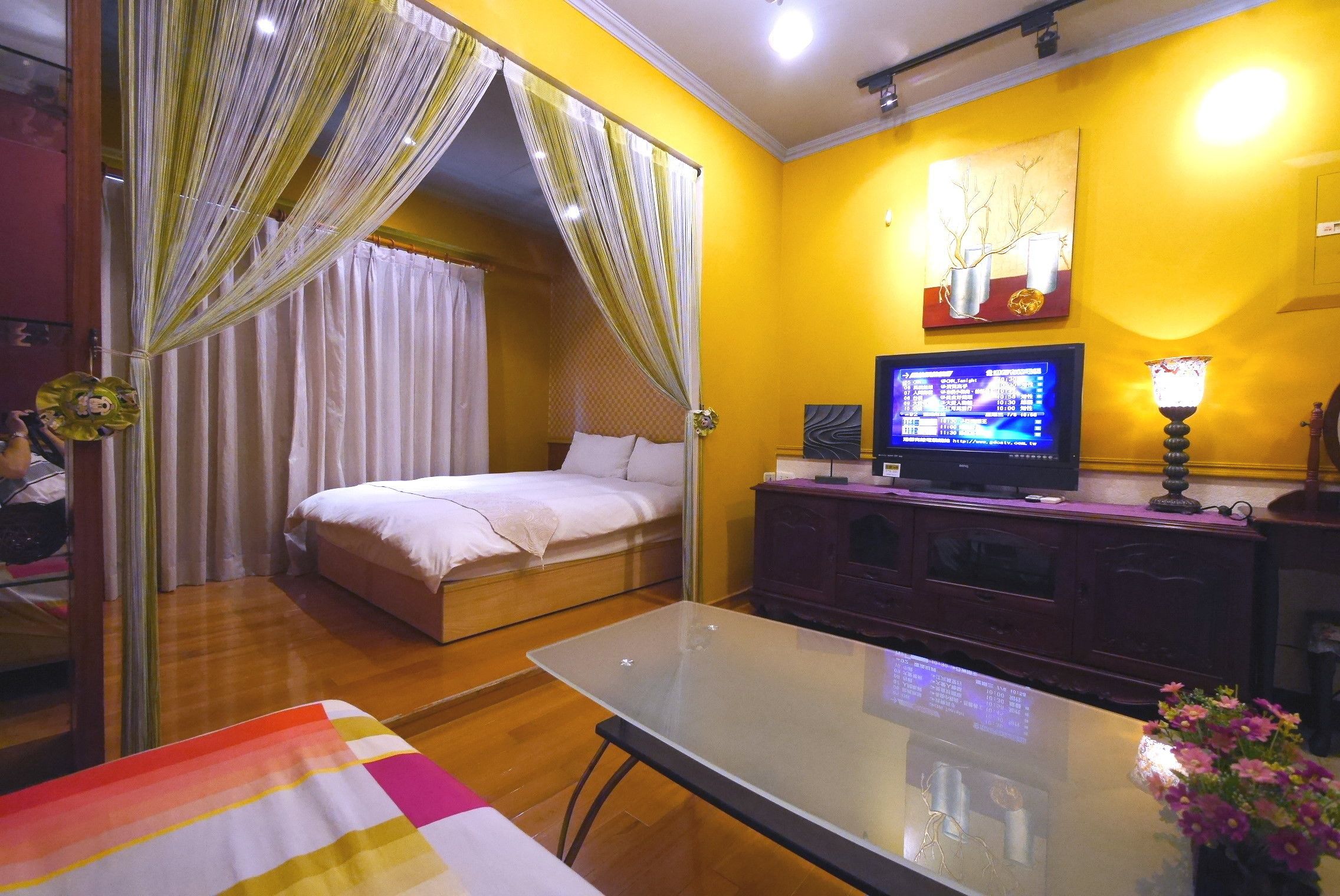 Una habitación con una cama, televisión, mesa y lámpara.