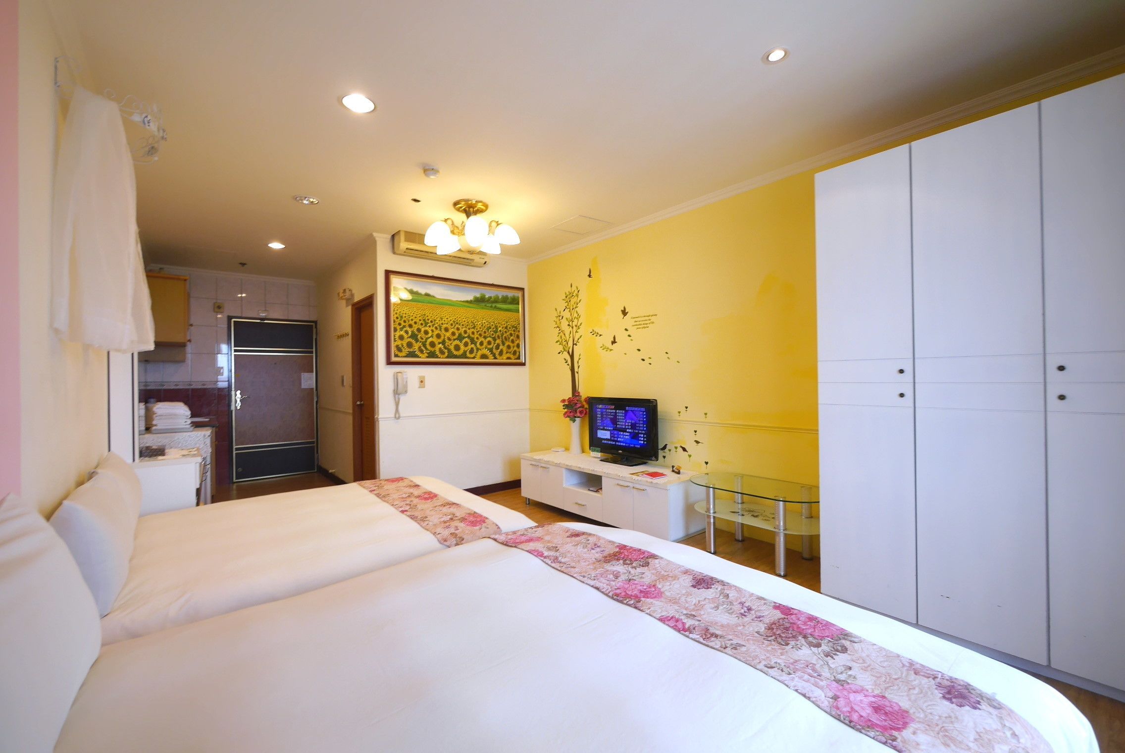 Ein Hotelzimmer mit zwei Betten, einem Fernseher, einer kleinen Küchenzeile und einem Kleiderschrank.