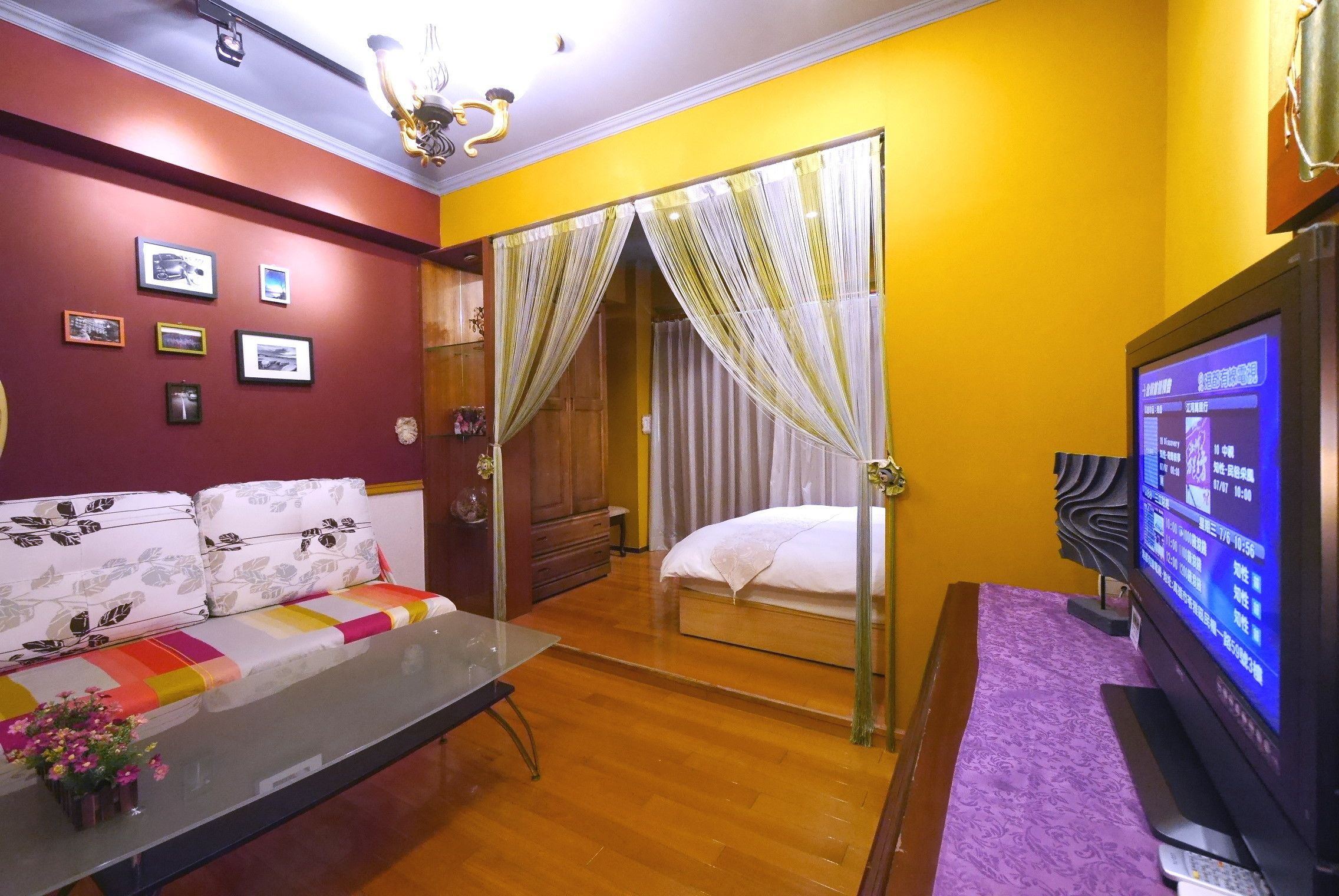 Une chambre d’hôtel avec un canapé, une table basse en verre, un téléviseur et un lit doté de rideaux.