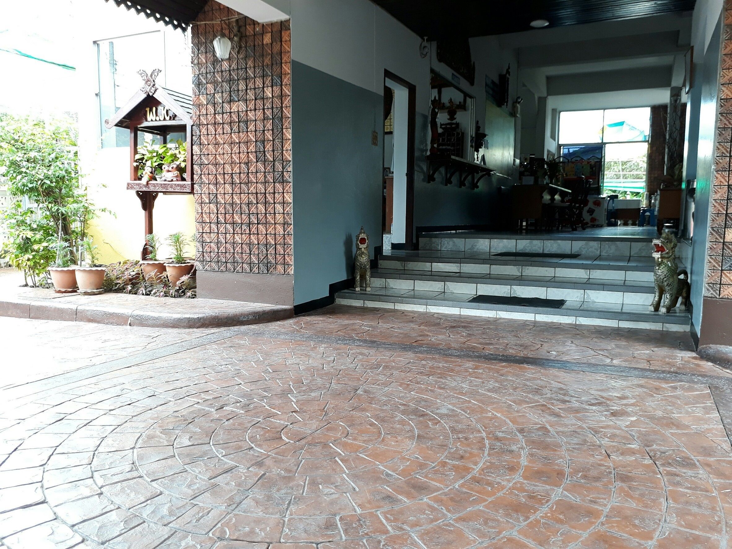 A building entrance with a tiled floor, steps leading up to a door, and potted plants outside.