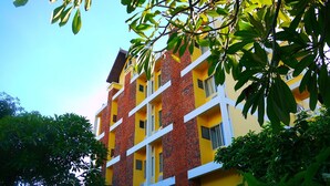 A multi-story building with yellow and red brick walls, white balconies, and surrounded by greenery. - Wiriya House (Chiang Mai)