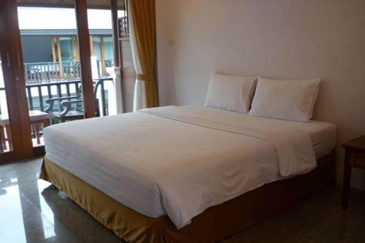 A hotel room with a large bed, a small bedside table, and a view of the balcony.