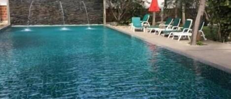 Una piscina con agua cristalina, rodeada de palmeras y sillas de descanso.