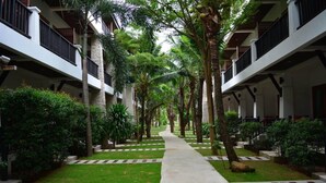 Um caminho ladeado por vegetação exuberante e edifícios brancos com varandas.