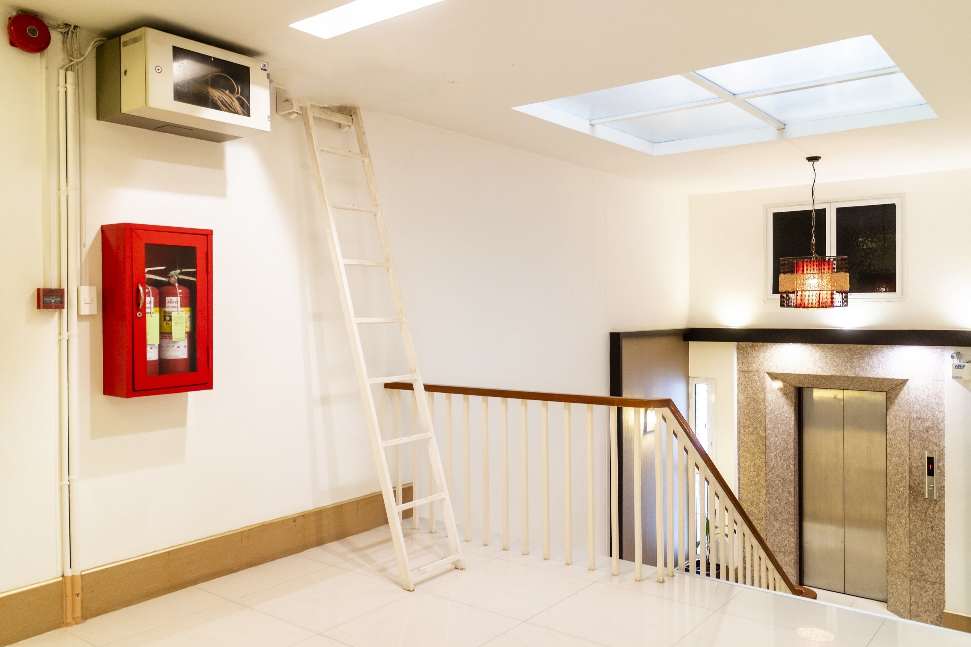 Una escalera con barandilla de madera, un extintor en gabinete rojo, un tragaluz y un moderno ascensor.