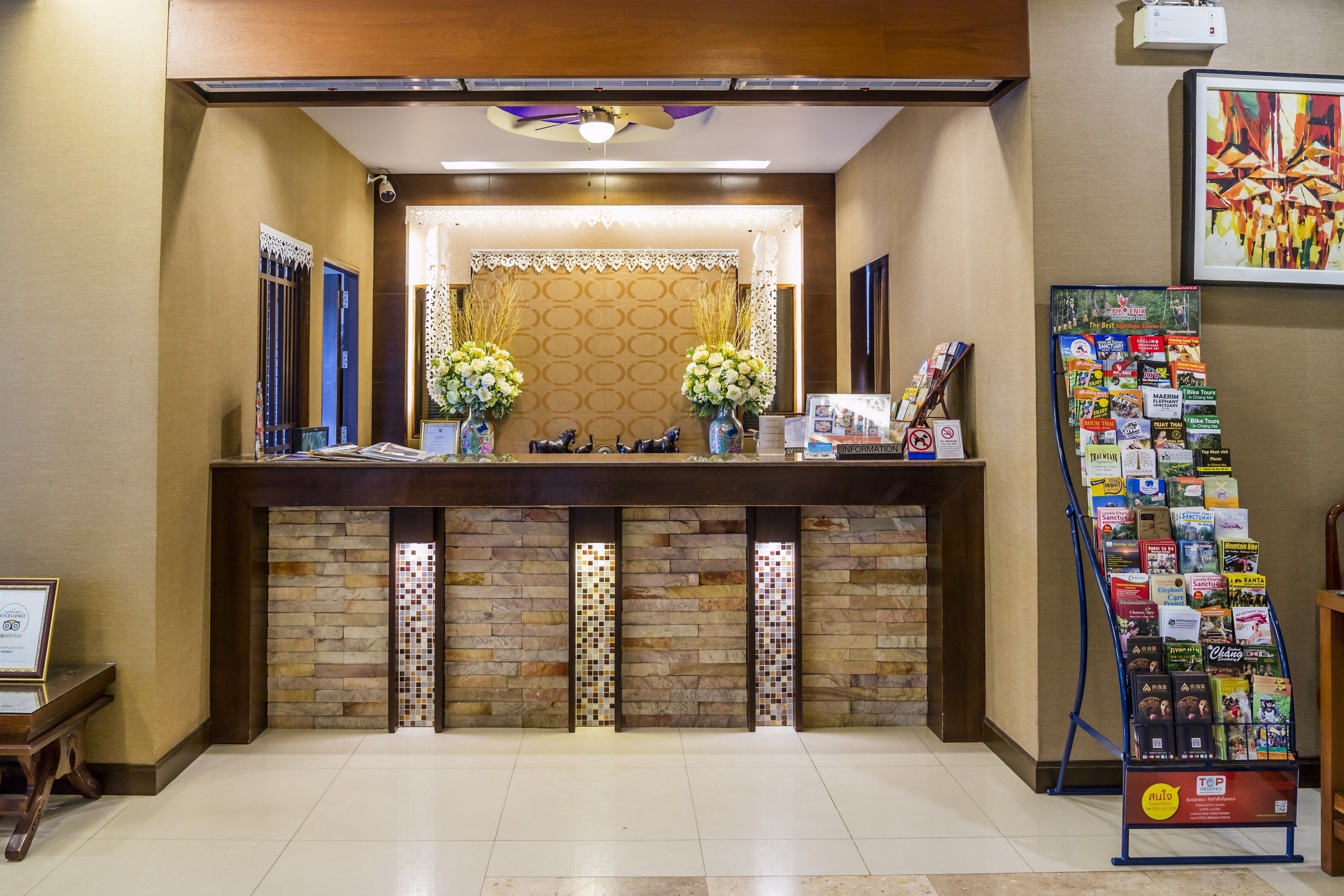 A reception desk with a tiled wall, two flower arrangements, and a display of magazines.