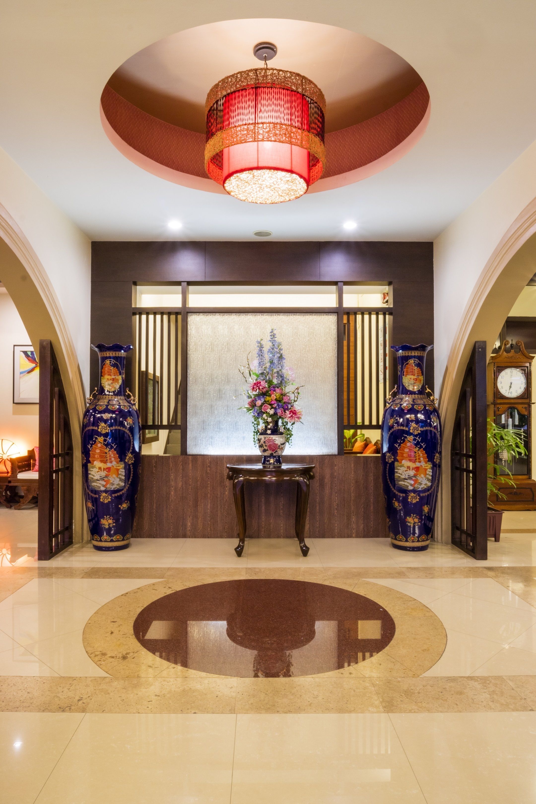 A lobby with a large circular rug, two ornate vases, a decorative chandelier, and a traditional clock.