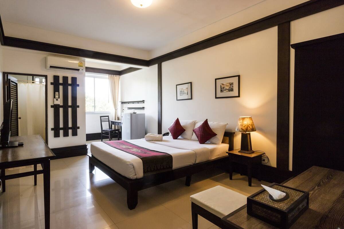 Una habitación de hotel con cama, mesita de noche, lámpara y una pequeña mesa con caja de pañuelos.