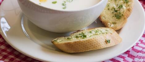 Un bol de soupe aux maïs et aux oignons verts, servi sur une assiette blanche, accompagné de deux morceaux de pain à l’ail, le tout posé sur une serviette à carreaux rouges et blancs.