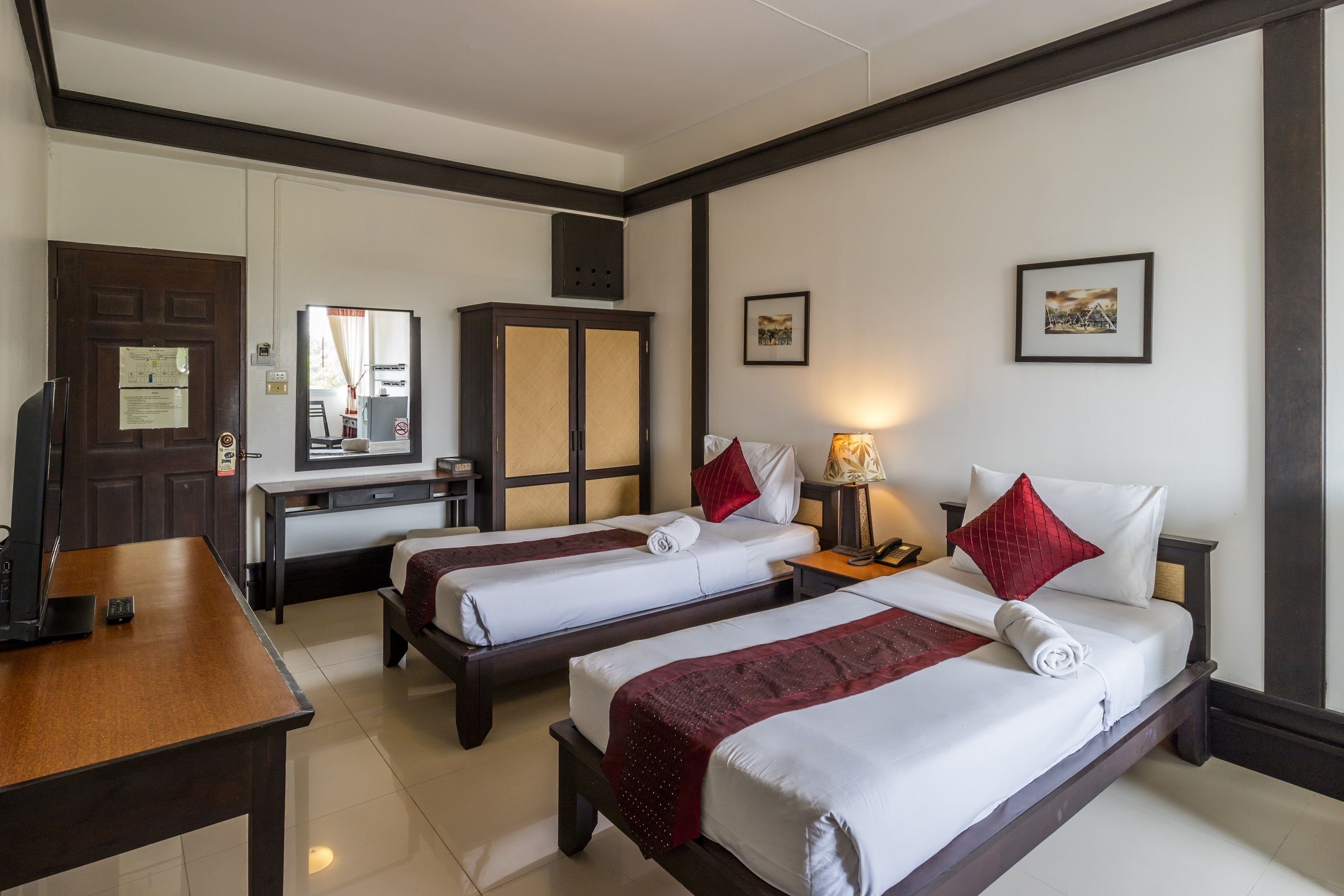 Une chambre d’hôtel avec deux lits, un bureau, une armoire et un miroir.