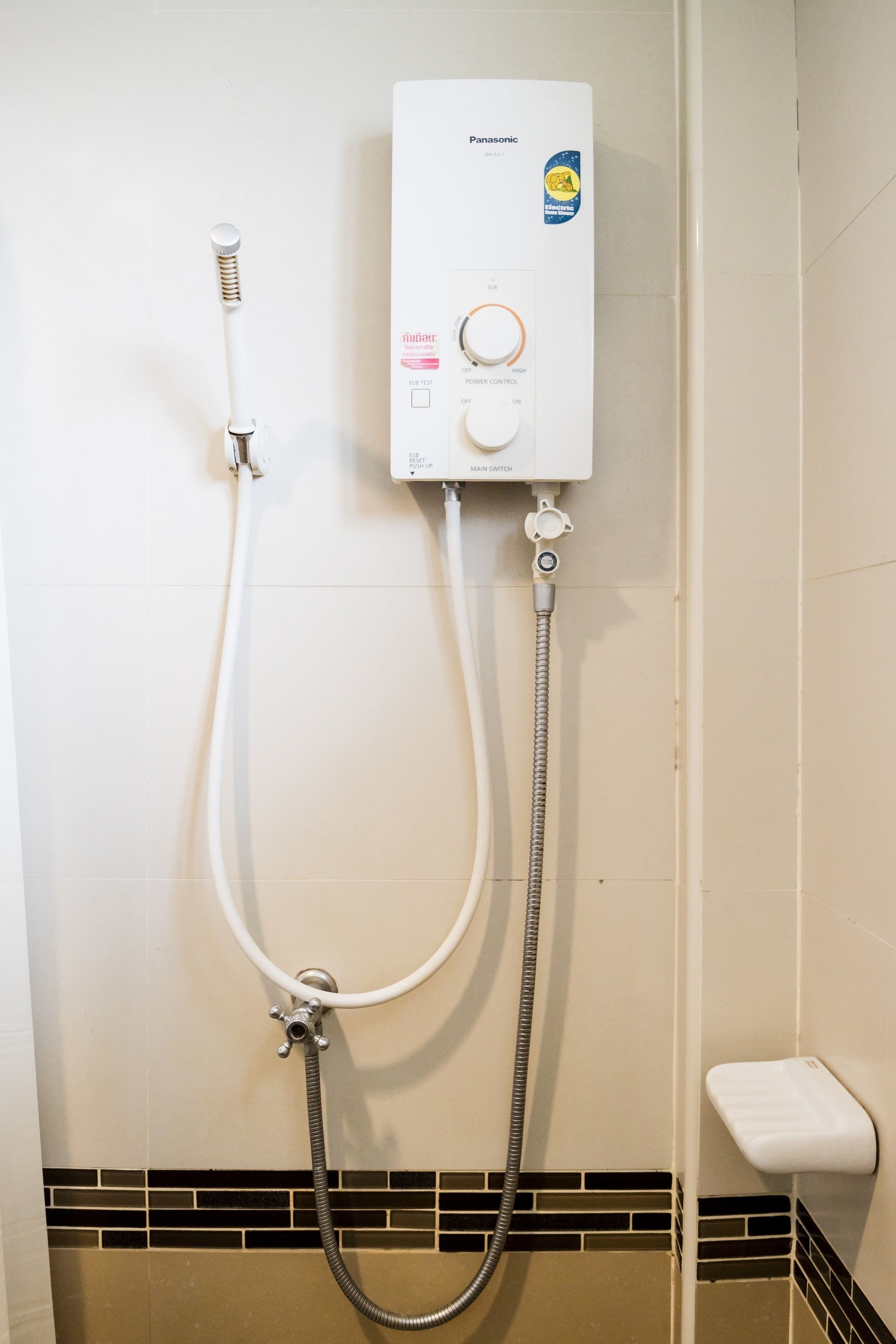 A bathroom with a white wall, a Panasonic electric shower, a white handheld showerhead, and a small white sink.