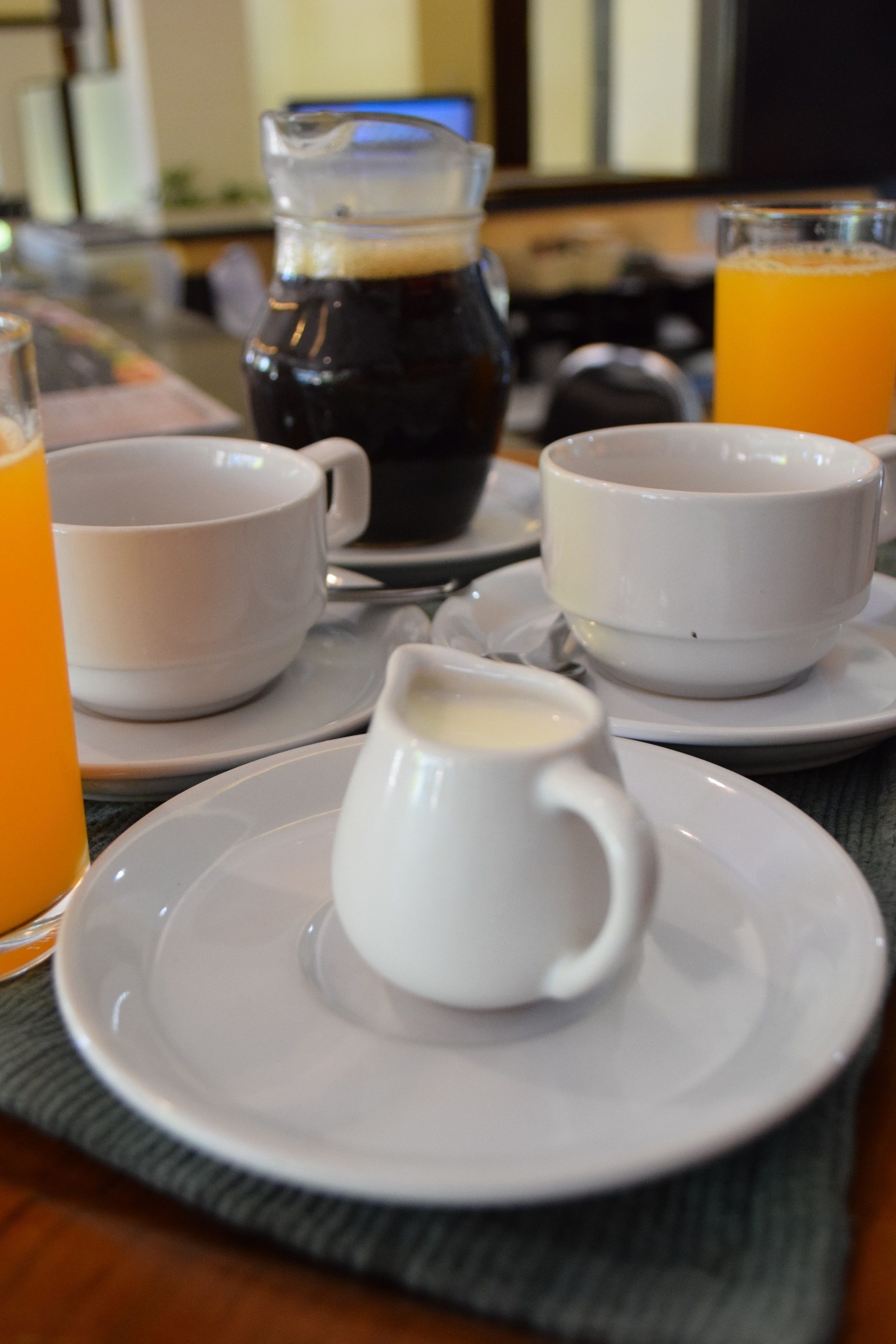 A breakfast setting with coffee, orange juice, and a pitcher of milk on a table.