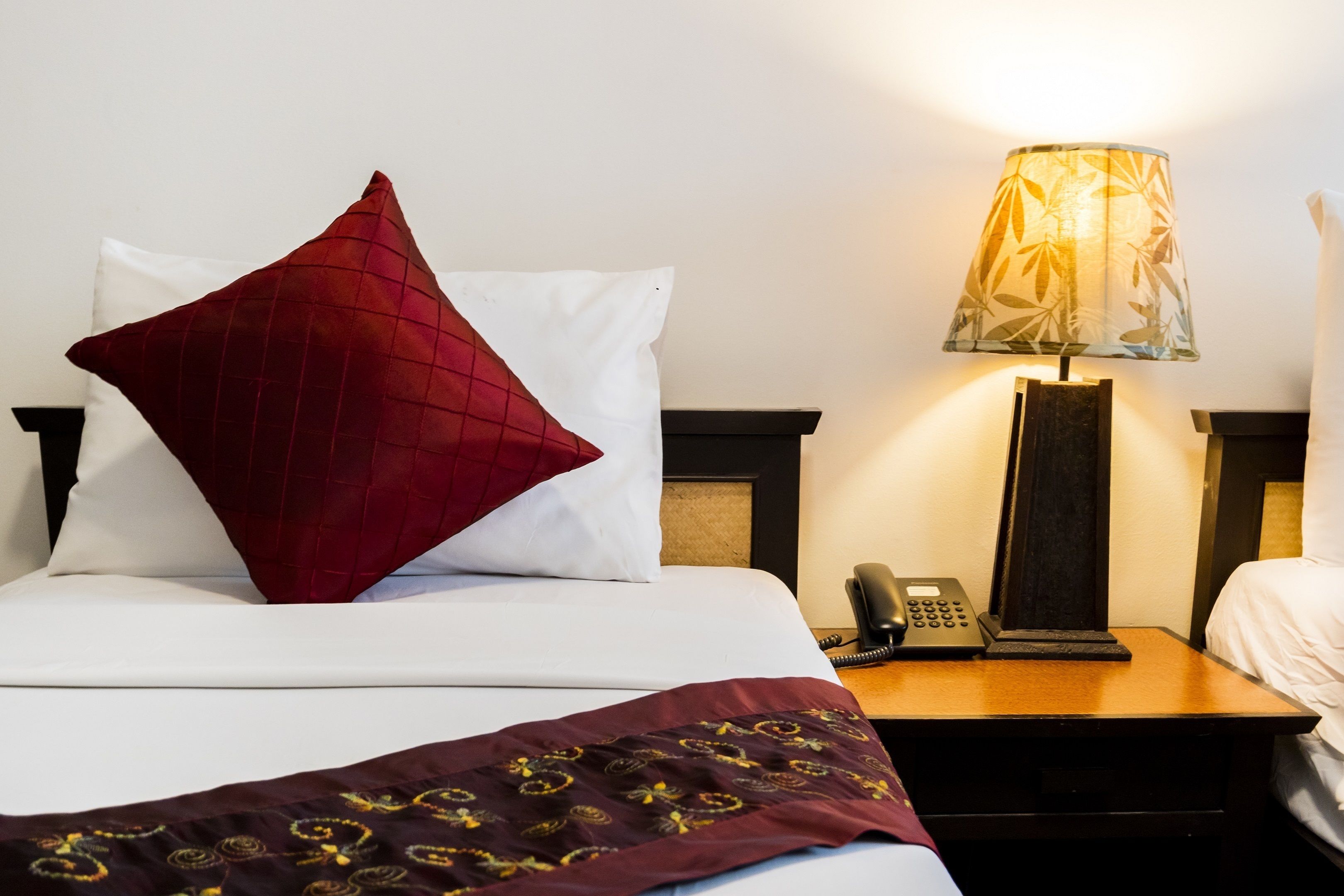 A hotel room with a bed, a red pillow, a white pillow, a lamp, and a telephone on a bedside table.