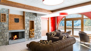 A modern living room with a stone fireplace, leather sofa, and a large window with a mountain view. - Résidence Lagrange Vacances Les Hauts de la Vanoise (Pralognan-la-Vanoise)