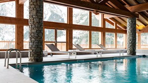 An indoor swimming pool with stone pillars, wooden beams, and large windows offering mountain views. - Résidence Lagrange Vacances Les Hauts de la Vanoise (Pralognan-la-Vanoise)