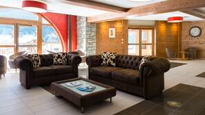 A spacious lobby with two brown leather sofas, a glass coffee table, and a stone wall. - Résidence Lagrange Vacances Les Hauts de la Vanoise (Pralognan-la-Vanoise)