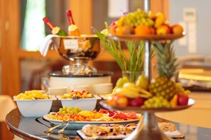 Una mesa de buffet con diversas frutas, una botella de champán y fuentes de comida.