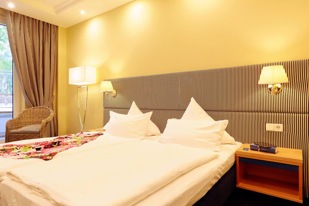 A hotel room with a large bed, two bedside lamps, a wooden nightstand, and a striped headboard.
