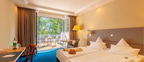 A hotel room with two beds, a desk, a chair, a table, and a view of the outdoors.