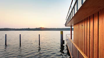 A wooden building with a deck extending over water, featuring a clear view of the sunset.